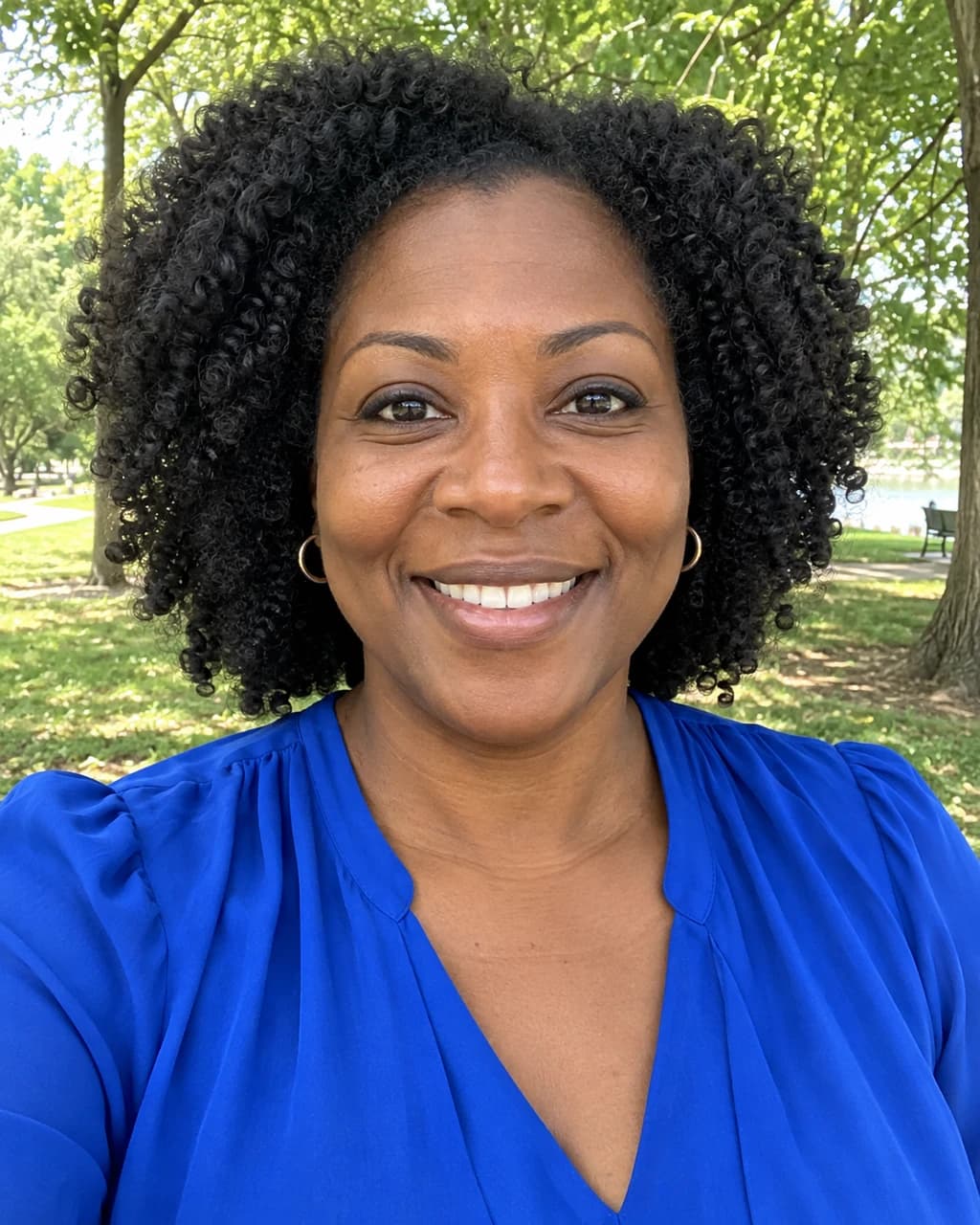 Example person 1: an AI-generated selfie of a woman in her forties with deep brown skin, black coily hair and dark brown eyes.