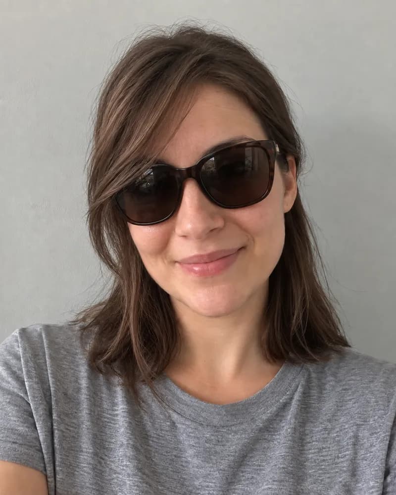 The same woman wearing dark sunglasses, with hair falling across her face.