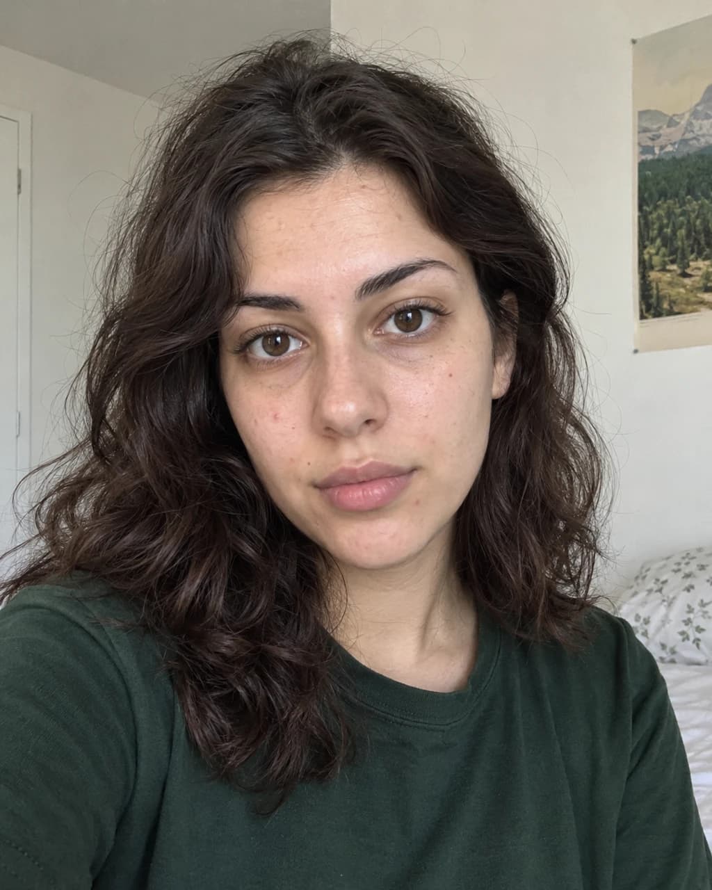 Example person 7: a selfie of a woman in her twenties with light olive skin and dark-brown wavy hair, in a forest-green t-shirt against a plain wall.